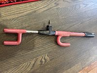 Full view of the red steering wheel lock with key inserted in the lock mechanism, showing the design and shape of the lock.