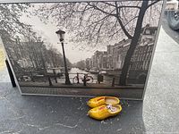 Framed black and white Amsterdam canal picture with a red bike in front with yellow Dutch clogs beside it on the pavement.