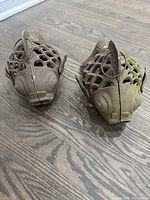 Two cast iron goldfish candle lantern holders with hanging rings, viewed from above and front showing fish faces and lattice openings.