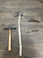 Full view of log marking hammer and three axe heads on wooden floor.