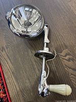 Full view of the vintage Unity police spotlight showing reflective lens, chrome body, mounting bracket, and white handle, laying on wooden floor.