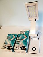 Photo showing two original boxes and one lamp folded open with lights visible showing the 24 LED arrangement, base, and flexible arm joints.