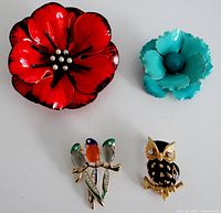 Top view showing all four brooches: large red flower, smaller blue flower, birds on branch, black and gold owl