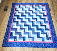 Full view of the blue rail fence quilt laid flat on a wooden floor.
