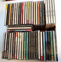 Top-down view of box showing 50 assorted CDs stacked upright side by side, spines visible with titles from various artists including jazz and orchestral music.