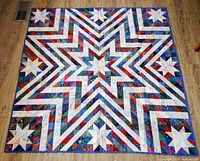 Full top-down photo of the quilt spread out flat, showing the large central star and surrounding smaller star motif design in various colors.