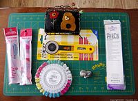 Full lot image with cutting mat, rotary cutter, pin cushion, thimble holder, pin wheel, fabric marker and quilting accessory shown arranged on the cutting mat.