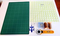 Full view of the sewing lot showing green cutting mat, Omnigrid ruler, rotary cutter, scissors, seam ripper, thread and pins