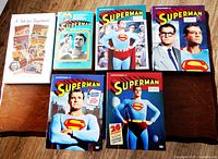 Photo of two hardcover books and four DVD box sets, titled and showing cover art related to Superman.