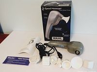 Overview of massager, power cord, 7 white attachments, instruction manual, and product registration card displayed in front of original packaging box