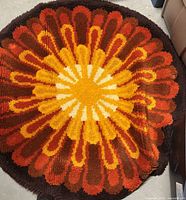 Top view of round 43 inch diameter rya rug displaying vivid sunburst floral pattern in warm tones of orange, yellow, brown.