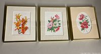 Three framed watercolour paintings of flowers arranged side by side on flat surface, each matted and framed in gold or light wood frames.