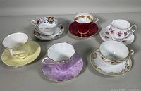 Six assorted vintage teacup and saucer sets with various colors and patterns displayed together.
