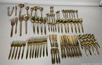 Full layout of flatware including forks, knives, spoons, and serving pieces with gold-tone finish and visible wear and tarnishing.