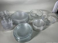 Overall set of embossed glass plates and bowls stacked on white surface, showing quantity and size ranges.