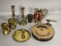 Full lot overview showing candleholders, plates stacked, pitcher, duck head bookends, small metal cup, and small metal object resembling iron.