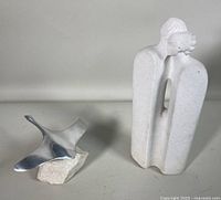 Porous stone sculpture of two human forms and aluminum Canadian goose sculpture mounted on rock base together in one photo.