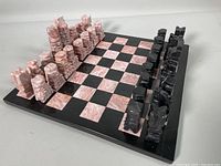 Full view of chess board with all 32 pieces arranged for play, showing black and pink marble squares and pieces.
