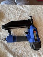 View of the blue and black Campbell Hausfeld pneumatic finish nailer with rubber grip and air hose connector.