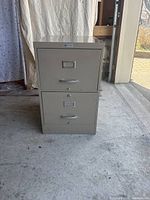 Front view of one beige metal filing cabinet with two drawers closed, showing minor scratches and dents.