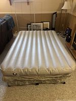 Beige double air mattress inflated and sitting on the collapsible metal frame base.