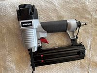 Husky brad nailer resting on bubble wrap surface, showing side view with black grip and red trigger.
