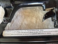 Close-up of specification label on pneumatic tool indicating compatible brads, 1/4" crown staples, and 18-gauge fasteners.