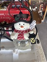 Individual close-up of one glass snowman outdoor light fixture showing detailed face, hat, scarf, and lantern