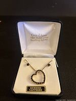 Photo of the open jewelry box displaying the heart-shaped sapphire necklace pendant and matching earrings with 'Cote d'Azur 18kt Gold over Sterling Silver' branding inside the lid and a 'Genuine Sapphire' label.