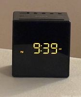 Front view of the black cube-shaped Sony digital alarm clock showing yellow LED time display 9:39 PM with DST indicator.