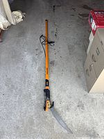 Full length view of orange and black Fiskars extendable tree pruner on concrete floor.