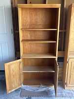 Full view of honey wooden bookcase showing three upper shelves and open lower cabinet with both doors open revealing interior shelf.