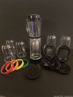 Photo of Magic Bullet blender base with small pitcher attachment, 5 colored rim cups, black lids, and blade attachments arranged on a surface.