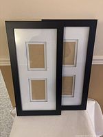 Two black wooden picture frames leaning against wall, each holds two photo inserts sized 4x8 inches.