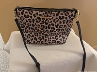 Front view of medium-sized pink and black animal print purse with gold-tone logo plate and zipper, black adjustable strap attached.