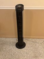 Full view of Seville Classics black and silver tower fan standing on carpeted floor.