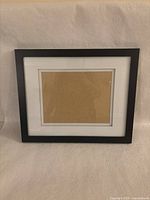 Front view of the black wood picture frame showing the white mat and cardboard backing visible inside.