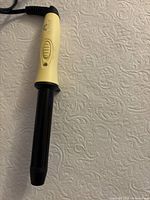 Close-up of Sutra Beauty Mini Curling Wand handle yellow with black barrel on textured surface
