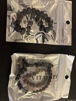 Two Vitality brand bead bracelets sealed in clear packaging with black lava stone and black, pink, and brown beads with metal spacers.