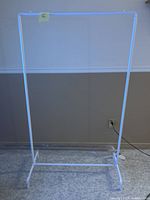 Full view of the white metal clothing rack standing upright with a plain wall background and minor signs of wear visible on the frame.