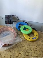 View of 3 electrical fish tapes in blue, green, and yellow, coiled copper tubing in plastic, and a black 13.8V power supply unit.