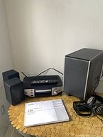 Photo showing the Denon S-302 main unit, remote, manual, headphones, and subwoofer.