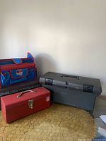 Two gray plastic tool boxes, one red metal toolbox, and blue fabric toolbox arranged on floor surface near wall