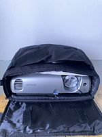 Epson projector enclosed in black carrying case with flap open showing the front including lens and vents.