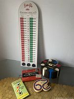 Vintage Sun-Glo shuffleboard scoring counter with red and green scoring columns, two knobs at bottom, next to round wooden holder for poker chips, vintage card games, and colorful token '29'.
