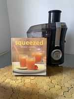 Front view of Hamilton Beach juicer with recipe book titled 'Squeezed'