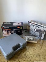 Photo showing all items including boxed steamer, boxed heat gun with metal nozzles, gray carrying case, and nailer.