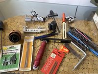 Overview of mixed hand tools including saw handles, screwdriver-type tools, small levels, files, hole saw blades, and bit sets on round wooden surface.