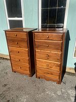 Pair of tall wooden dressers standing side by side outdoors in front of a building, showing front and side views.
