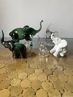 Group of six small elephant figurines of different materials on a table showing all items.